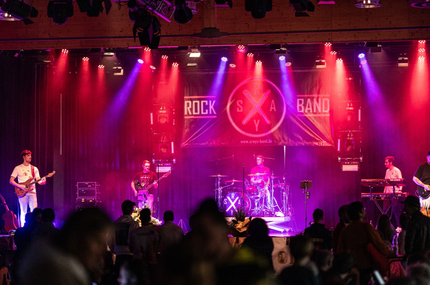 Band auf beleuchteter Bühne vor Publikum mit rot-violetter Lichtshow